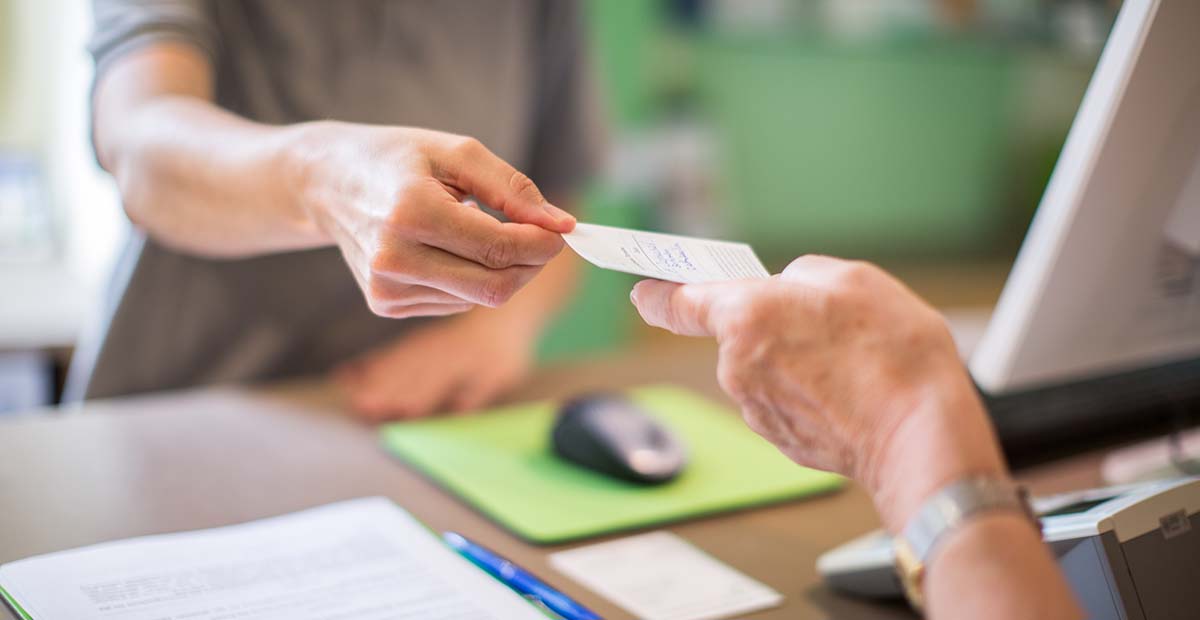 Person behind a desk handing a slip of paper to another
