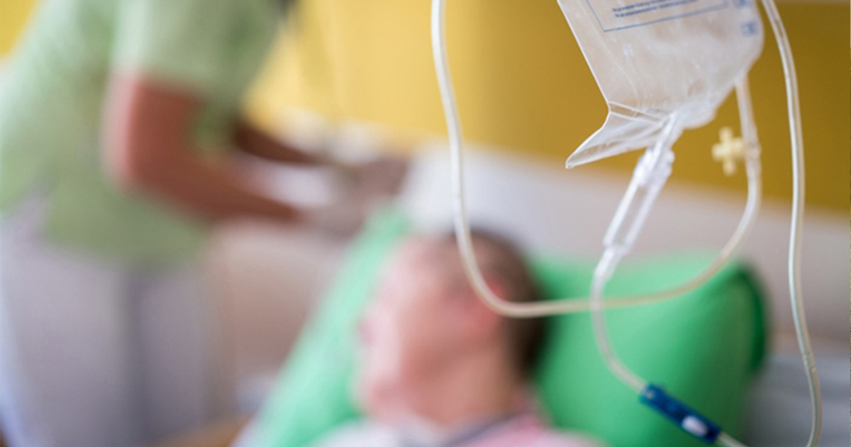 Infusion bag in foreground with patient and infusion nurse in background