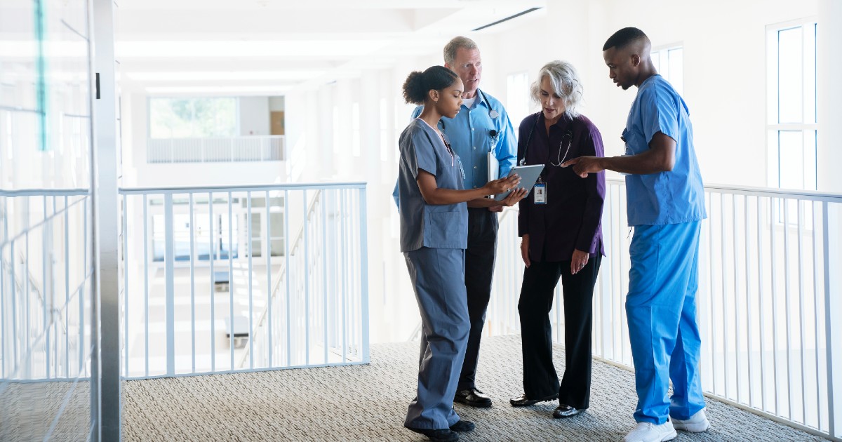 Nurses huddled together look at electronic health records on a tablet.