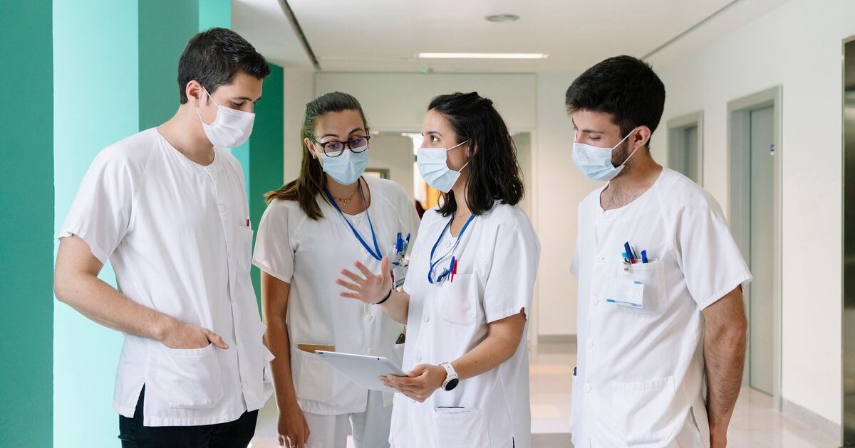 One healthcare worker talks with colleagues and references data on a tablet.