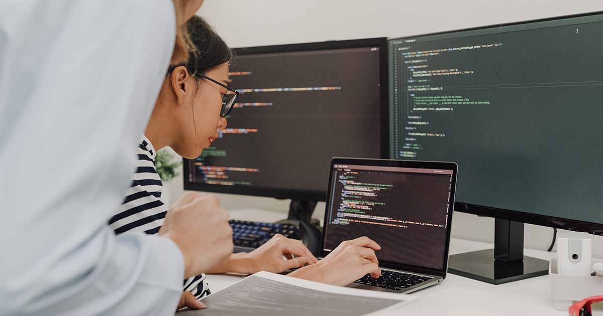 Workers coding on a laptop with dual monitors