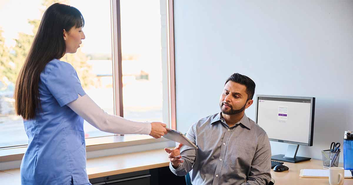Healthcare worker hading tablet to person at a desk