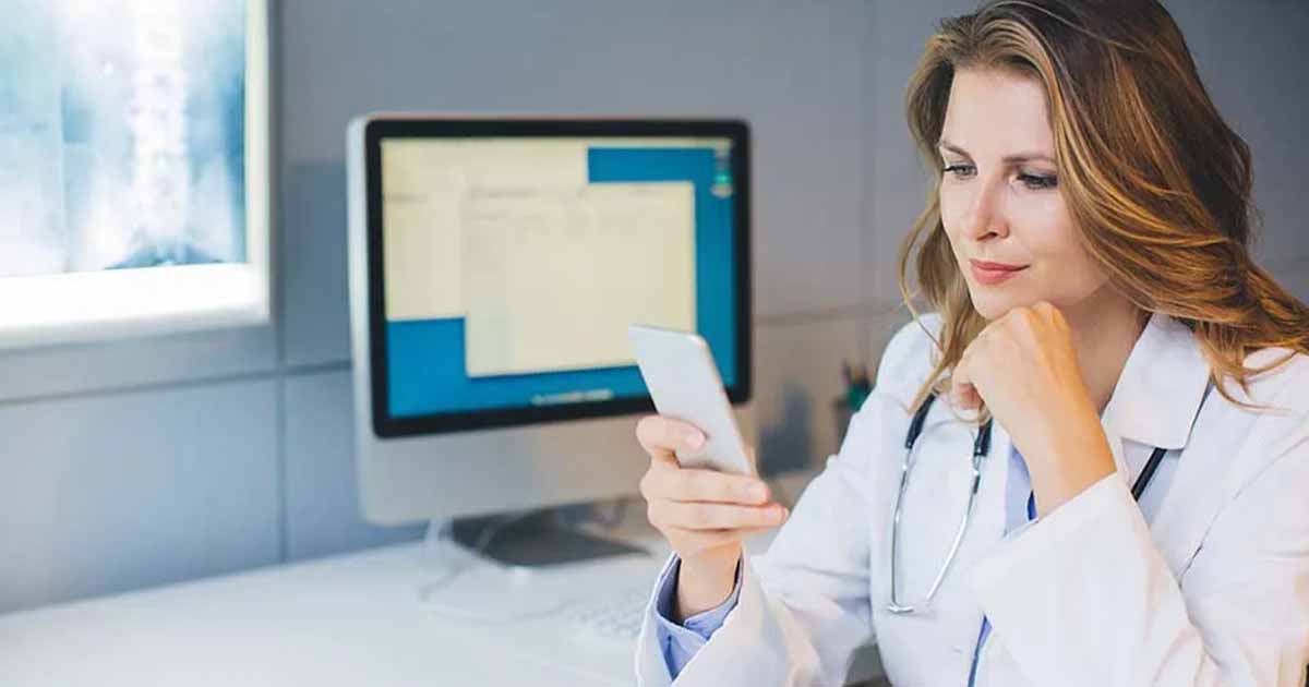doctor at her office sitting at the table and using smart phone