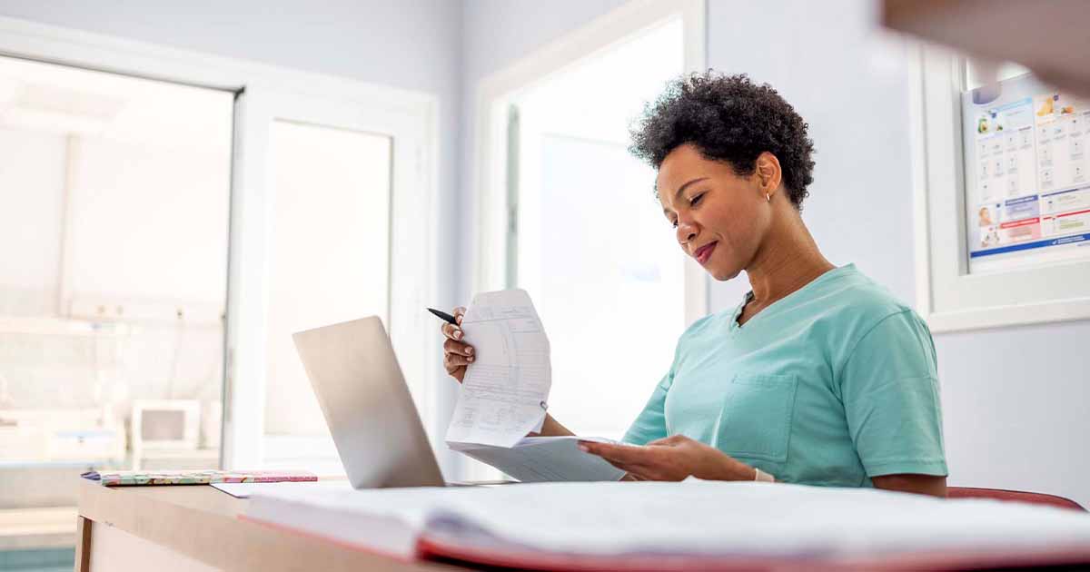 Healthcare worker looking at papers at a desk with a laptop