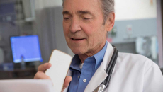Gray-haired doctor sitting at a monitor and talking into a cell phone