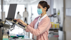 A nurse checking a patient's file on a laptop mounted in a hospital corridor