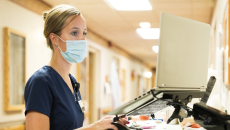 A nurse accessing a patient's record in a laptop in the hospital corridor