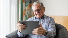 Person with gray hair and glasses surfs looking at a tablet
