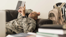 Male soldier lays on a couch reading a notebook.