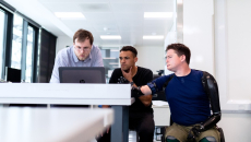 Three people in an office sit looking at a computer