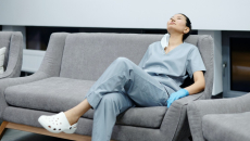 Female nurse in grey scrubs on rests on a couch with her head back