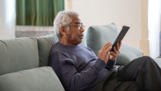 Person in a blue shirt sits  with a tablet on a couch