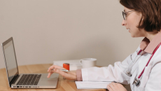 A doctor holding a pen is using a laptop