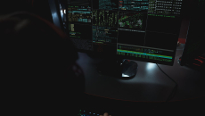 A shadowed figure views a computer terminal monitoring data streams.