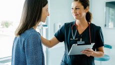 A nurse holding a digital tablet talks to a patient in bed