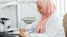 A nurse wearing hijab is filling out a patient form