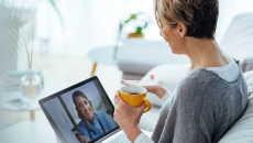 A patient holding a cup of coffee in a virtual call with their doctor