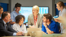 A group of healthcare professionals are meeting in front of a laptop to discuss cybersecurity.