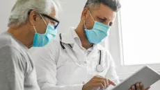 Doctor and patient wearing masks look at a tablet in an exam room