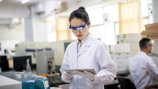 A scientist in a lab gown holding a digital tablet