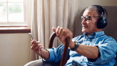 An elderly person using a smartphone and headphones sitting on a chair