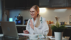 A doctor in a kitchen conducting a virtual consultation on a laptop computer