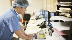 Healthcare worker in scrubs and a hair net using a computer