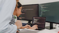 Workers coding on a laptop with dual monitors