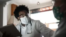 Doctor in mask with a tablet talking to patient