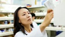 Pharmacist takes a prescription from a shelf and reads it  