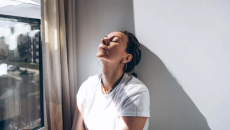 Stressed woman sits with her head against a wall 
