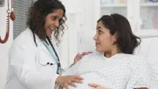 Doctor talking to pregnant patient and placing had on stomach