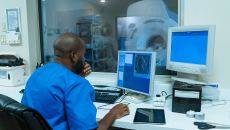 Healthcare worker looking at computer screen with MRI room in background