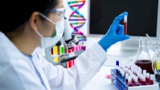Masked healthcare worker holding vial of blood in lab