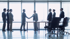 People standing in front of a window shaking hands while other people are watching