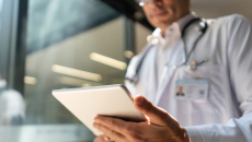 Healthcare provider wearing a lab coat and stethoscope while looking at a tablet