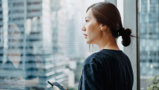 A person holding a smartphone staring outside the office window