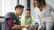 A doctor explaining to a patient and their carer their diagnosis using a digital tablet