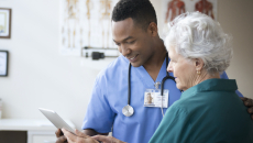A nurse helping an elder patient use a digital tablet