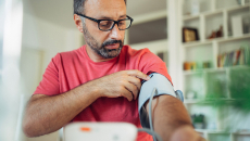 Man in a red tshirt measures his blood pressure with an RPM device.