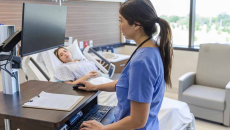Nursing using laptop in hospital room with patient