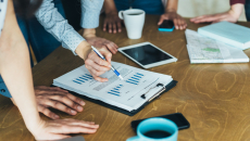 group of people with one person pointing at graph on a clipboard