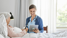 caregiver at patient bedside reviews prescription information with a virtual care prescriber on a tablet