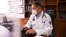 Male doctor in a medical mask works at his desktop.