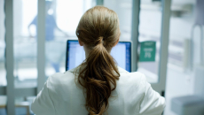 Doctor with long hair in a ponytail sits and works on a laptop