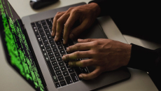 Hands work at a laptop showing code onscreen.