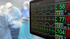 ECG monitor appears in the foreground and surgeons appear to be operating in the background.