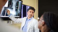 Radiologist points to image on screen during a consultation with fellow clinicians