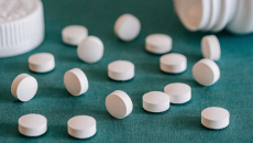 Pills lay on a surface with an open prescription bottle in the background