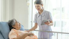 A nurse holding a digital tablet is assisting a patient lying in bed